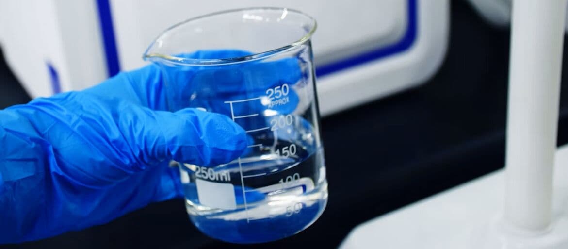 Gloved technician holding a laboratory beaker