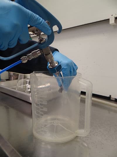 Technician pressure-rinsing a component for cleanliness testing